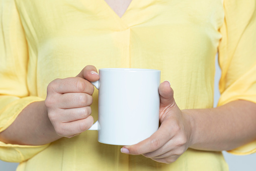 Unrecognizable caucasian female wearing yellow t-shirt is holding a coffee mug in hands.