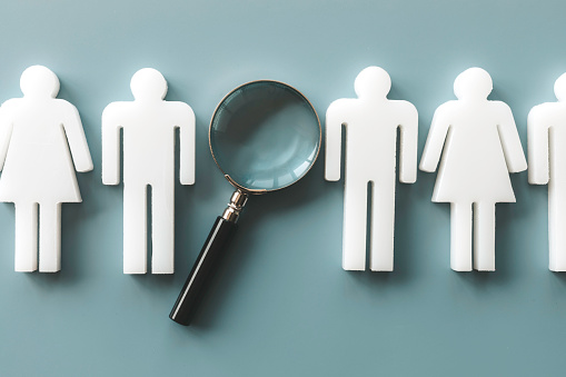 Recruitment, human resource and survey concept . Represented by a row of man and woman models in a row and one magnifying glass on blue background.