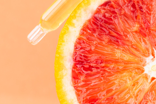 Front view of pipette with serum above sliced grapefruit .