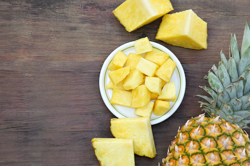 Cut and whole ripe pineapples on wooden table, flat lay. Space for text