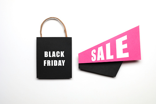 Black shopping bag, pink and black  papers with announcement effect and Black Friday Sale text on it on white background.