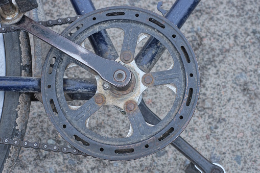 a black metal pedal with an asterisk and a chain on the iron frame of an old bicycle lies on gray asphalt on the street