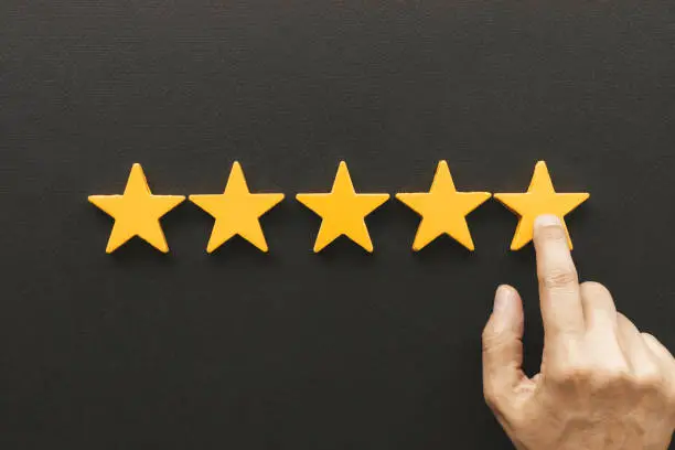 Five star rating feedback. Hand is pointing at last yellow star shape in front of black background. Giving best score point to review the service