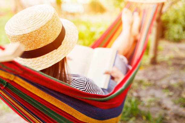 istock Young woman reading book while lying in comfortable hammock at green garden 1500099873