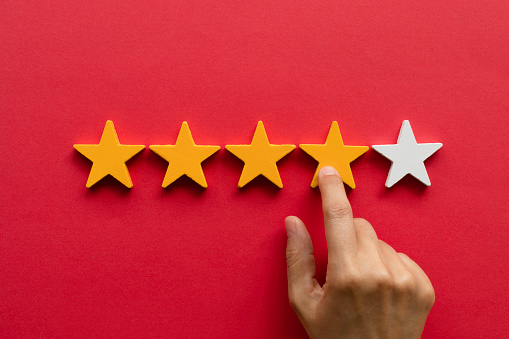 Five star rating feedback. Hand is pointing at fourth star shape in front of red background. Giving score point to review the service