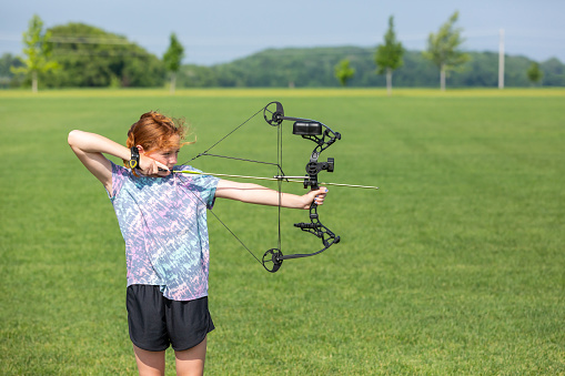 Girl practicing archery with her bow outdoors on a summer day.