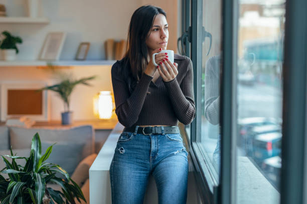 istock Beautiful thoughtful woman drinking a cup of coffee while looking forward next to the window at home 1500107957