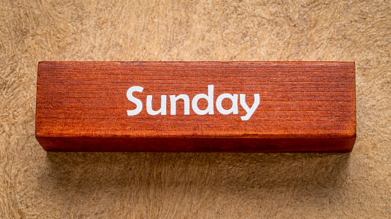 Sunday text on wooden block against handmade bark paper in earth tones, calendar concept