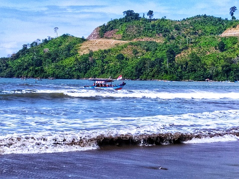 the appearance of a boat heading towards the beach with the accompaniment of the waves against the background of the hills in sunny day