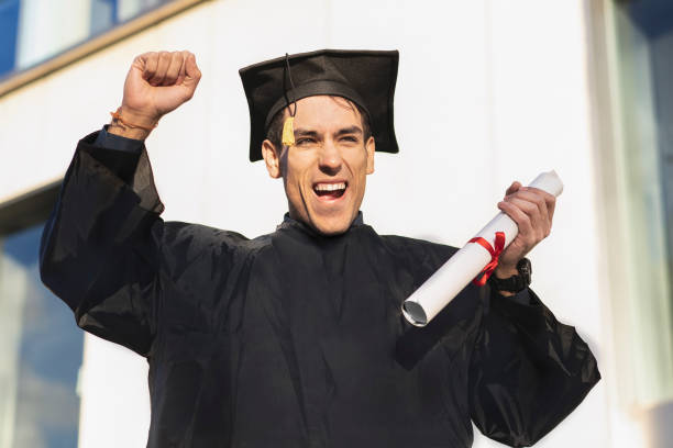 istock Happy young man wearing graduation robe holding diploma while raising his arm 1500127265