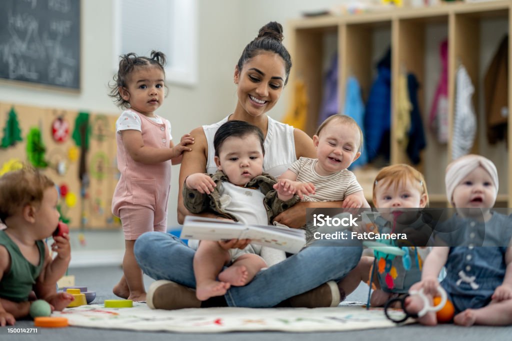 ChildcareTeacher with Children A childcare provider of Indian decent, sits with a large group of babies as she read them a book in their classroom. Child Care Stock Photo