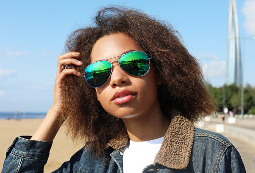 Young afro woman wearing sunglasses with perfect teeth and dark clean skin having rest outdoors