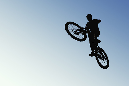 A cyclist mid-jump, in silhouette against the open sky. The image captures the thrill of cycling