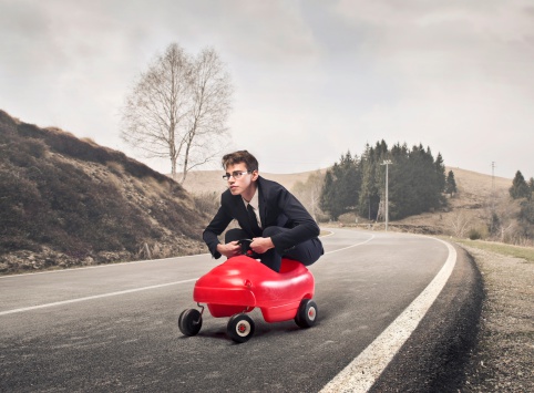 Young businessman driving a toy car on a country road