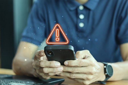 Notification smartphone concept. A young man using a phone with a warning symbol indicating the risk of data theft, Hacking passwords, and personal data.