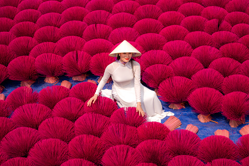Vietnamese girl in traditional white Ao dai dress with incense drying outdoors in Hanoi, Vietnam
