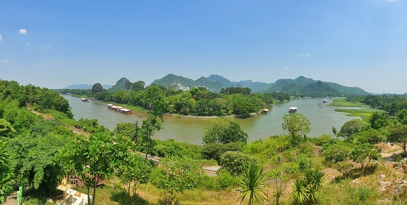 Panoramic picture of the river from a high angle. Overlooking the water bend, 2 boats are sailing down the river. Overlapping mountain views, blue sky, no clouds, greenery fresh air