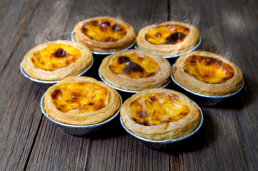 egg tart in aluminum foil cup with smoke\non wood table