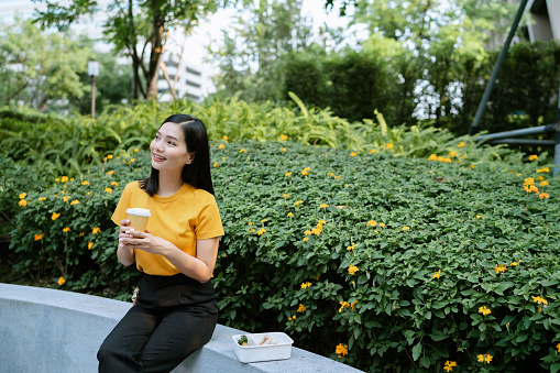 An Asian office worker enjoying a simple lifestyle by having a homemade dinner in a community park after work.