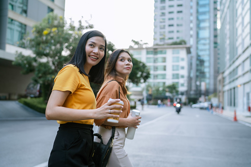 Two Asian women having a pleasant conversation while walking along the city street together.