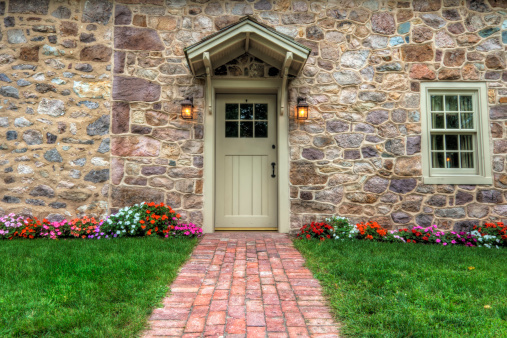 Path and door entrance of a stone home with spring flowers and lush lawn.