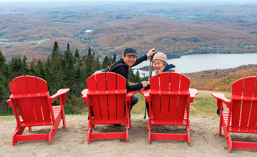 Senior Chinese woman and son sitting on red chairs and posing for photos at Mont Tremblant summit. Quebec. Canada.