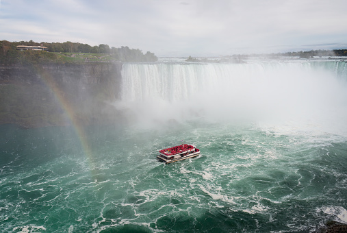 Rainbows and cruising boat at Niagara Falls. Tourists wearing pink raincoats on the boat. Canada.