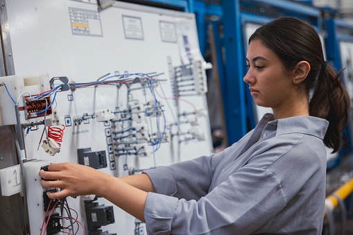 Professional young industrial factory woman employee working with machine parts putting, checking and testing industrial equipments cables in large Electric electronics wire and cable manufacturing plant factory warehouse