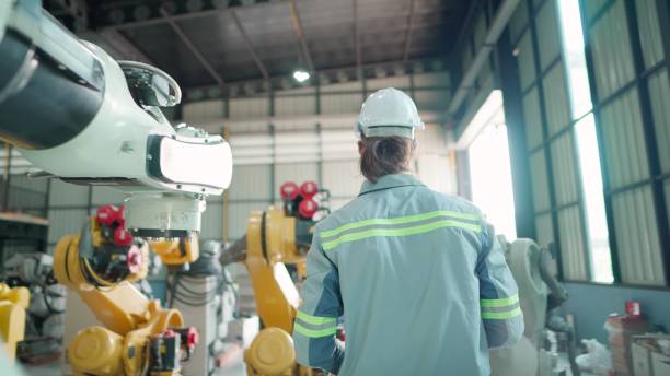 istock Rear view. Male engineer or technician wearing safety uniform working in robotic arm production line, inspection the quality to meet the standards  or test the operation before shipping at factory.  Employee working in a robotic warehouse at manufacturing 1500212500