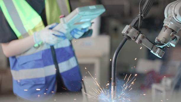 Professional  female engineer or technician uses control panel to control the operation of the robot arm system welding work piece and control quality operate process work heavy industry. Smart industry robot arms for production technology in factory.