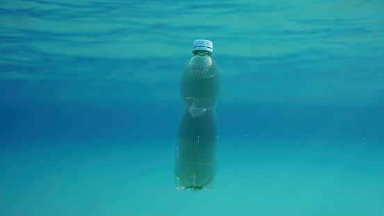 Green plastic bottle drifting under surface of blue water. Plastic pollution of Ocean, Discarded plastic bottle floats underwater in sunlight, Red sea, Egypt