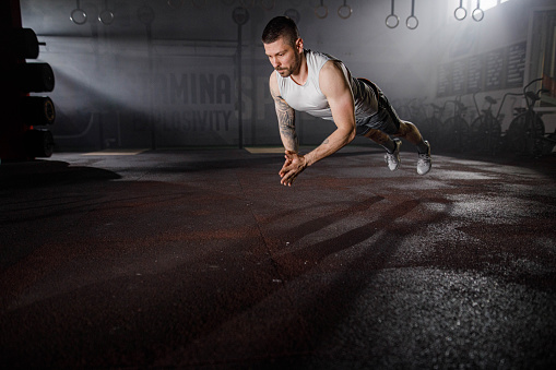 Young athletic man exercising push-ups while clapping his hands in a gym. Copy space.