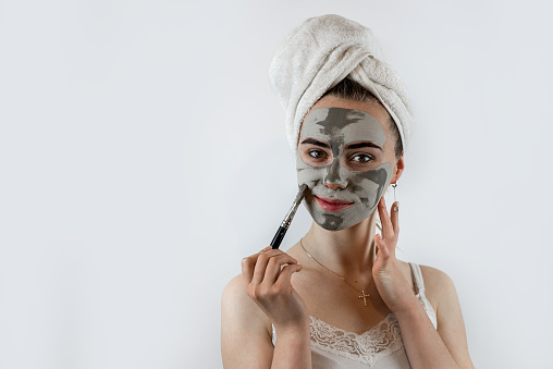 Pretty woman applying with brush clay or mud facial mask isolated on white. Beauty spa treatment