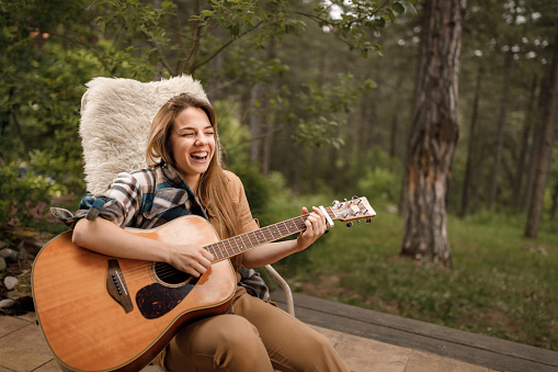 Cheerful woman having fun while playing a guitar on a patio.