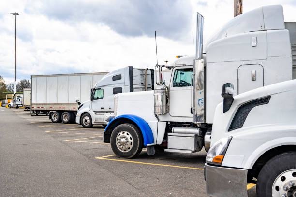 istock Different make and models of white big rig semi trucks with semi trailers standing in row on truck stop parking lot for truck driver rest 1500225240