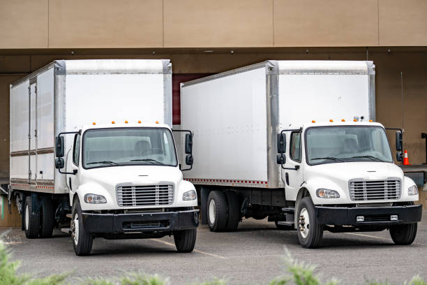 istock Two middle day cab semi trucks with box trailers standing on the warehouse dock loading cargo for the next local delivery 1500226361
