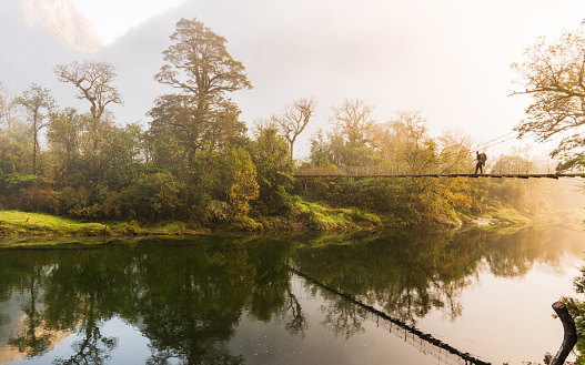 Early morning at Milford Track and hiker crossing suspension bridge with a majestic view in Fiordland National Park, South Island, New Zealand.