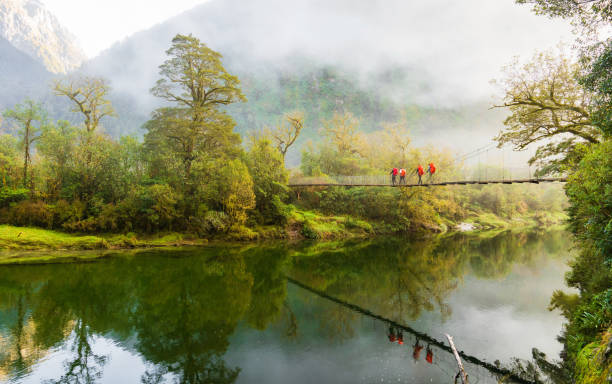 Early morning at Milford Track and hikers crossing suspension bridge with a majestic view in Fiordland National Park, South Island, New Zealand.