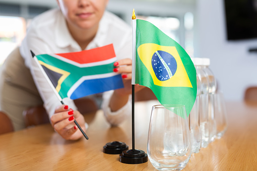 Little flag of Brazil on table with bottles of water and flag of South Africa put next to it by positive young woman in meeting room