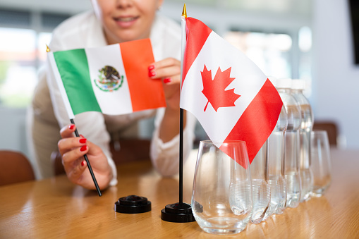 Young woman in business clothes puts flags of Mexico and Canada on negotiating table in office