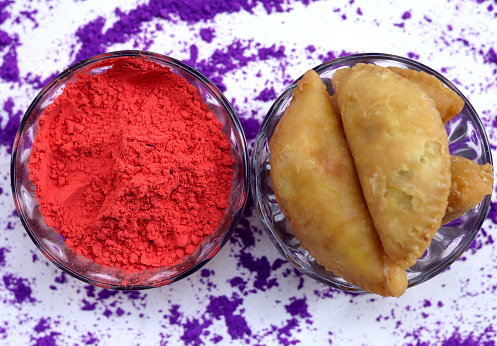 Gulal (Colored Powder), and Gujia in bowl on white background. Holi is a popular and significant Hindu festival celebrated as the Festival of Colours, Love and Spring. It celebrates the eternal and divine love of the god Radha and Krishna.