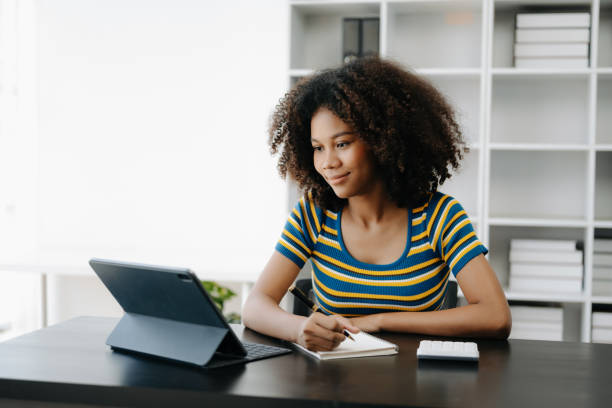 istock Beautiful African woman using laptop and tablet while sitting at her working place. Concentrated at work in home office 1500231283
