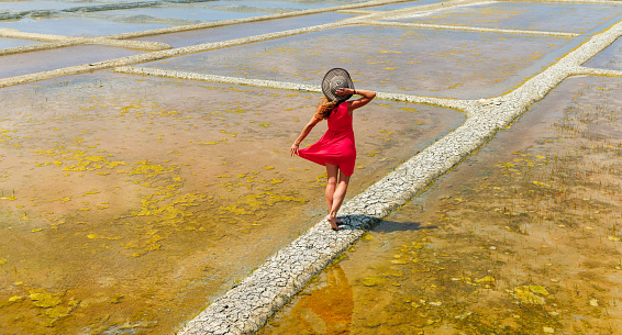 Woman tourist with red dress walking in salt marsh in Guerande,  Saline- Loire Atlantic,  Pays de la Loire in France