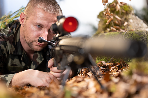 Hunter is hidden in the forest and shooting with sniper rifle, autumn hunting season.