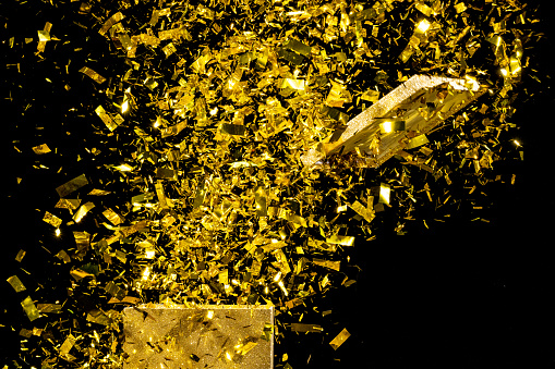 Close-up of exploding gold coloured confetti against black background.