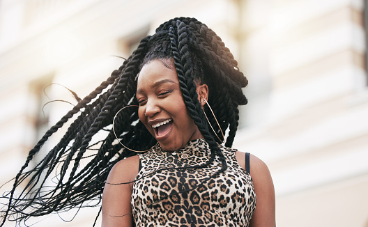 Hair, freedom and fashion with a fun black woman in the city on a summer day feeling cheerful or carefree. Braids, free and trendy with a young female in town on an urban background with flare