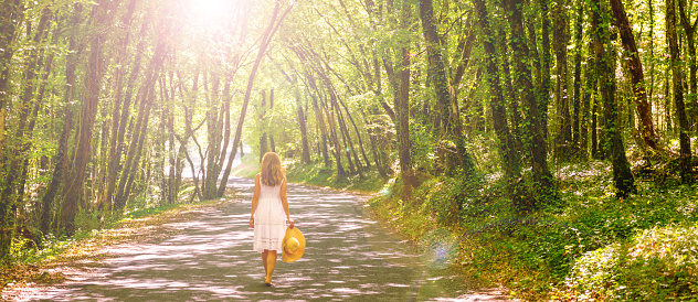 Woman wearing white dress walking in forest with sunlight