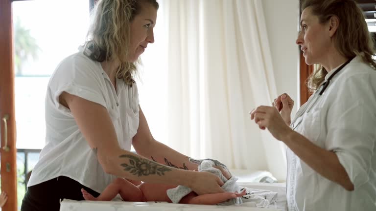 Doctor, healthcare and a mother dressing her baby while listening to medical advice in her home. Family, medicine and children with a medicine professional talking to a mom about newborn infant care