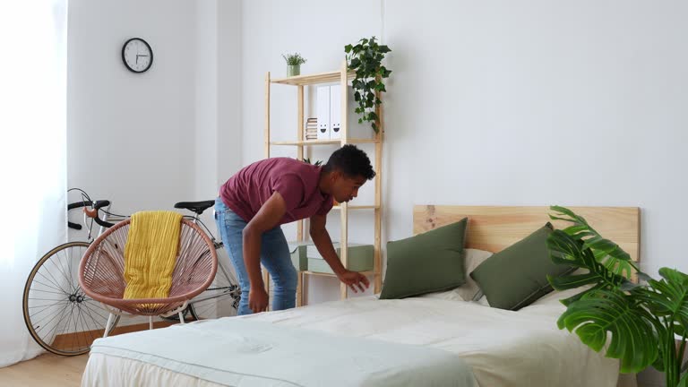 Young man making the bed in his room.