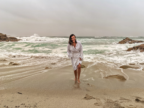 Woman walking along the edge of the beach in a bathrobe on a cold cloudy day